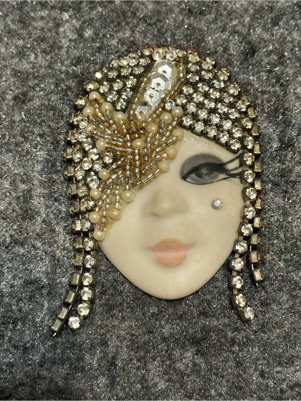 This is a vintage porcelain flapper face brooch adorned with sparkling rhineston